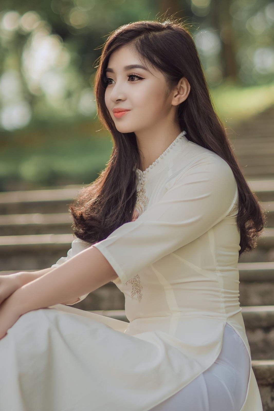 Feminine Asian model with long dark hair posing outdoors in an elegant white dress